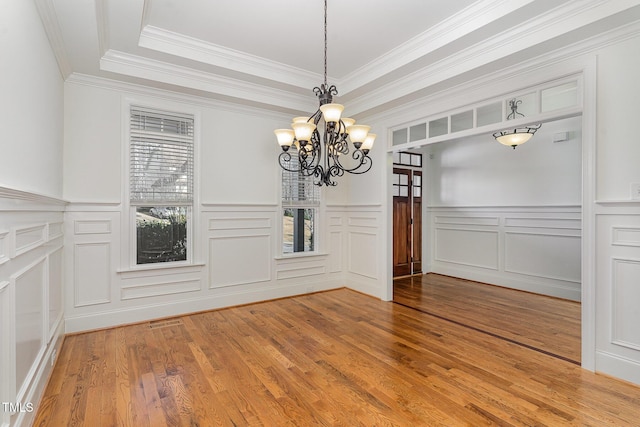 unfurnished dining area with an inviting chandelier, crown molding, wood-type flooring, and a raised ceiling