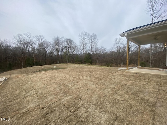 view of yard with a view of trees and ceiling fan