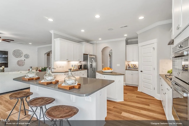 kitchen with light wood finished floors, a center island, open floor plan, arched walkways, and stainless steel appliances