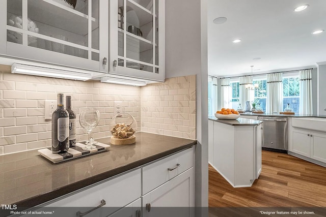 kitchen with wood finished floors, white cabinetry, glass insert cabinets, dishwasher, and dark countertops