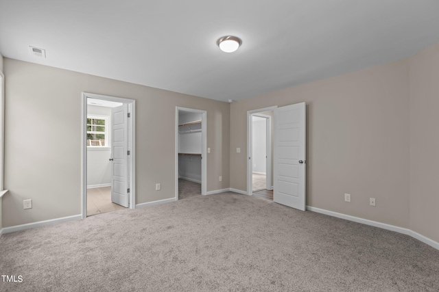 unfurnished bedroom with connected bathroom, light colored carpet, a spacious closet, and a closet