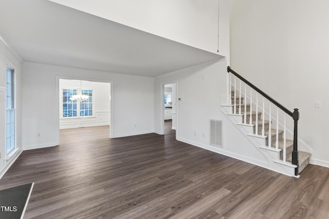 unfurnished living room featuring a chandelier, crown molding, and dark wood-type flooring