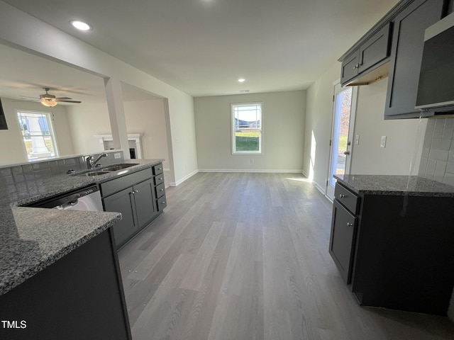 kitchen featuring dishwasher, sink, light wood-type flooring, tasteful backsplash, and stone countertops