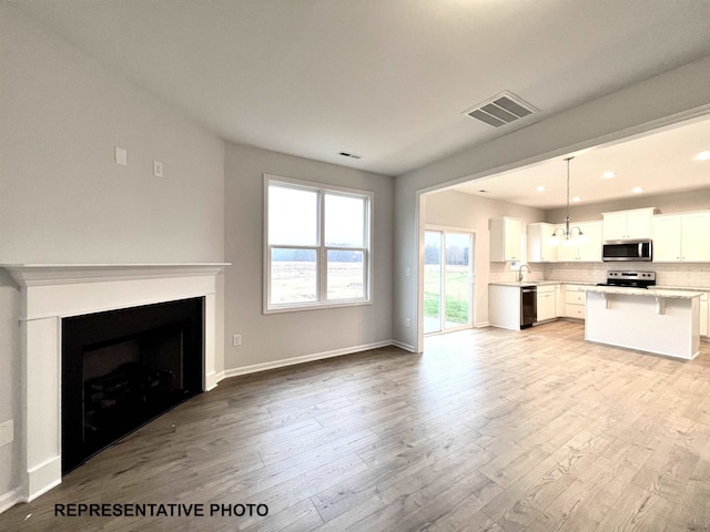 unfurnished living room featuring light wood-type flooring, visible vents, a sink, a fireplace, and baseboards