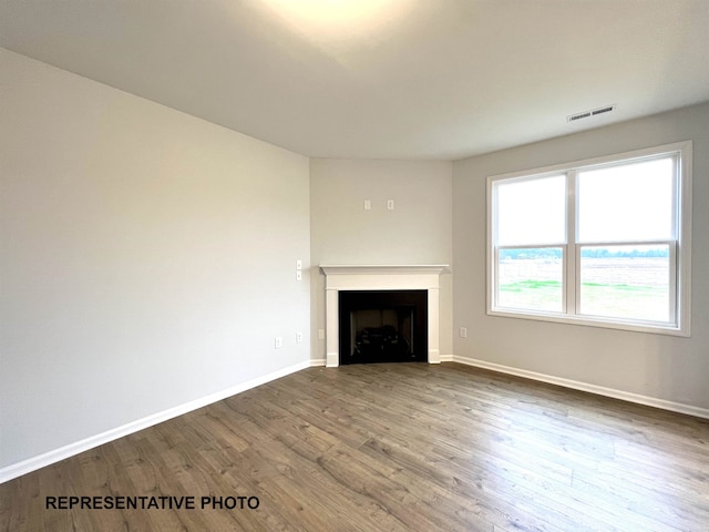 unfurnished living room with a fireplace, visible vents, wood finished floors, and baseboards