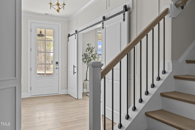 foyer entrance featuring crown molding, visible vents, stairway, light wood-style flooring, and a barn door