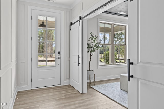 entryway with visible vents, a barn door, light wood-style flooring, and baseboards