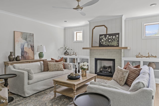 living area with a fireplace, a ceiling fan, crown molding, and wood finished floors