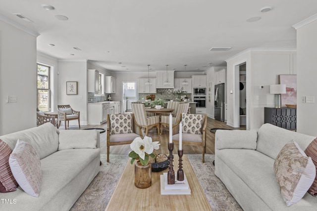 living area with visible vents, light wood-style flooring, and crown molding