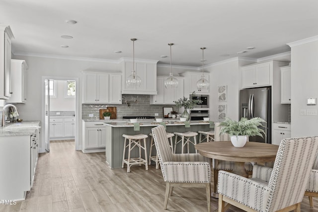 kitchen with a kitchen island, a sink, white cabinetry, appliances with stainless steel finishes, and tasteful backsplash