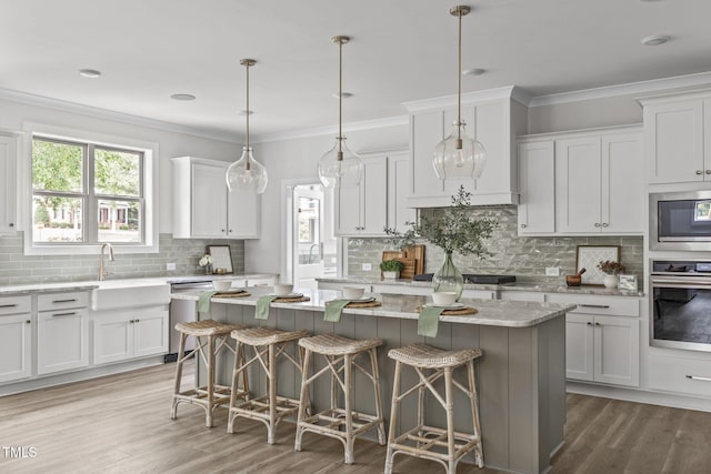 kitchen with a kitchen island, white cabinetry, appliances with stainless steel finishes, light wood-type flooring, and crown molding