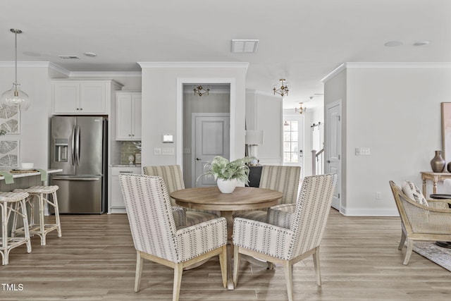 dining space with baseboards, visible vents, ornamental molding, light wood-style floors, and a chandelier