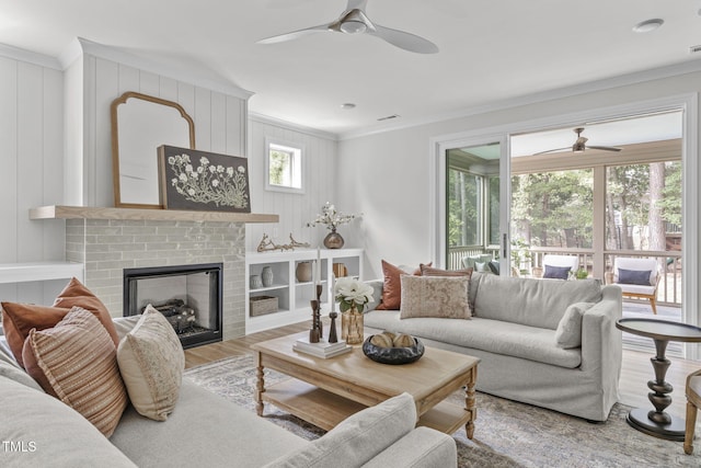 living area with a brick fireplace, crown molding, ceiling fan, and wood finished floors