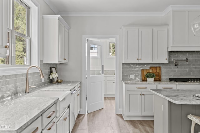 kitchen featuring white cabinets, black stovetop, crown molding, light wood-style floors, and a sink