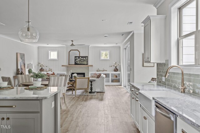 kitchen with a fireplace, a sink, ornamental molding, stainless steel dishwasher, and light wood-type flooring