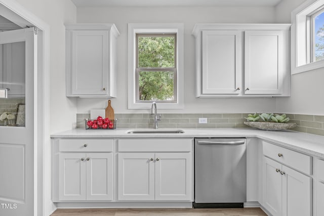 kitchen featuring white cabinets, dishwasher, light countertops, a healthy amount of sunlight, and a sink