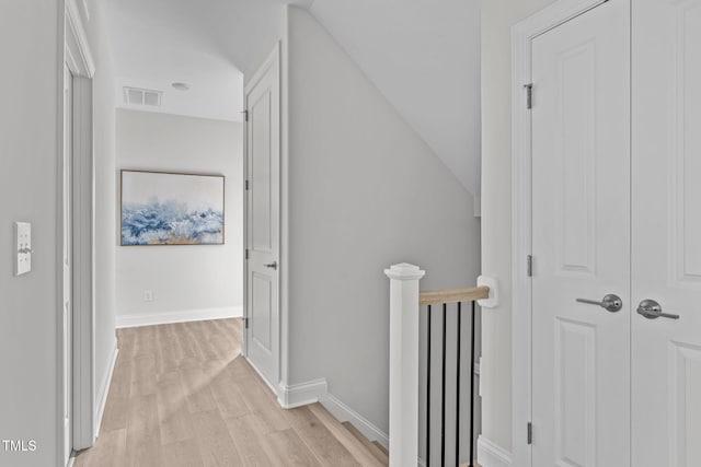 hallway featuring baseboards, visible vents, light wood-style flooring, and an upstairs landing