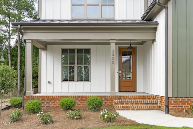 view of exterior entry with board and batten siding, a standing seam roof, covered porch, and metal roof