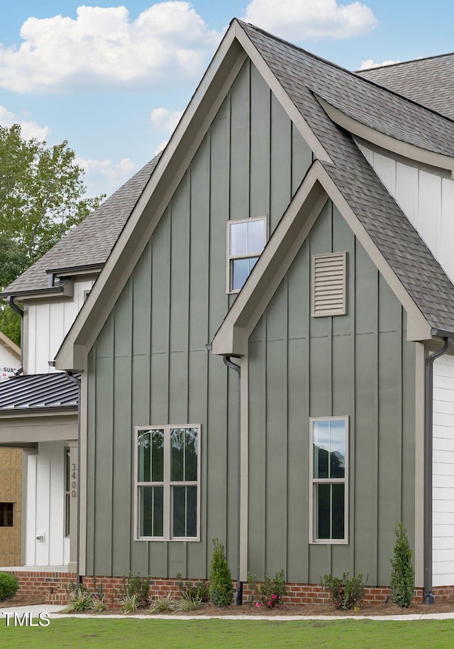 view of side of home with metal roof, a yard, a shingled roof, and board and batten siding