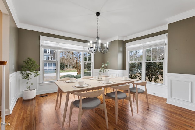 dining space featuring wood-type flooring, ornamental molding, and a notable chandelier