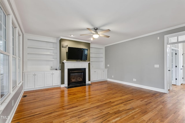 unfurnished living room with a wealth of natural light, built in shelves, light hardwood / wood-style floors, ceiling fan, and crown molding