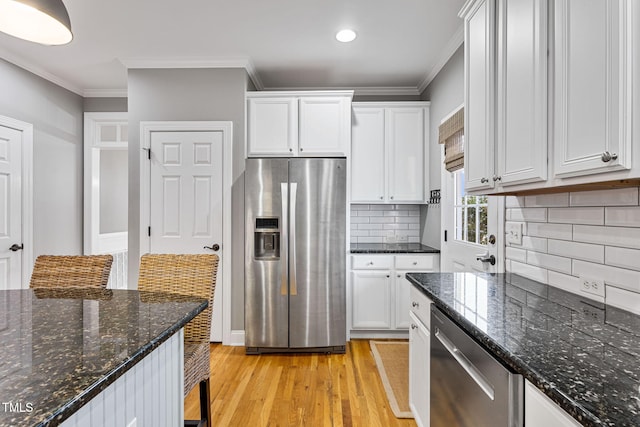 kitchen featuring white cabinets, tasteful backsplash, light wood-type flooring, dark stone countertops, and stainless steel appliances