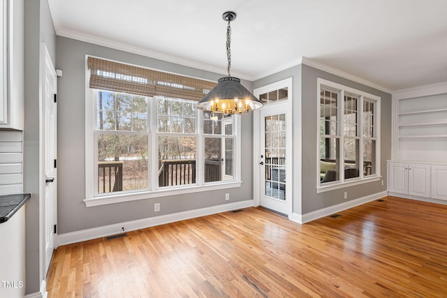 unfurnished dining area with built in features, crown molding, a chandelier, and light hardwood / wood-style flooring