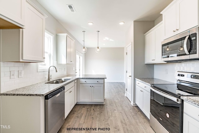 kitchen with pendant lighting, sink, appliances with stainless steel finishes, white cabinetry, and light hardwood / wood-style floors