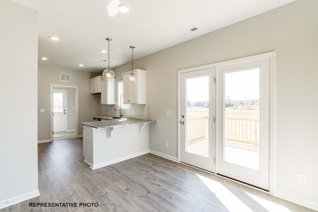 kitchen featuring decorative light fixtures, a breakfast bar area, white cabinets, light hardwood / wood-style floors, and kitchen peninsula