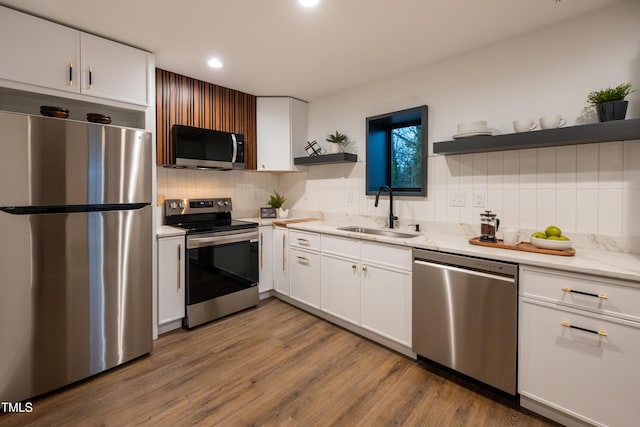 kitchen with white cabinetry, sink, light stone counters, appliances with stainless steel finishes, and light wood-type flooring