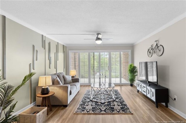 living room featuring a textured ceiling, light wood-type flooring, ceiling fan, and ornamental molding