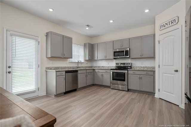 kitchen with appliances with stainless steel finishes, light hardwood / wood-style flooring, gray cabinetry, and light stone counters