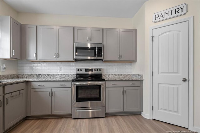 kitchen featuring gray cabinetry, light stone countertops, backsplash, and appliances with stainless steel finishes