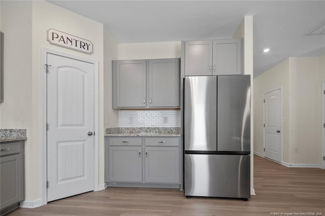 kitchen with light stone countertops, stainless steel fridge, tasteful backsplash, and gray cabinetry