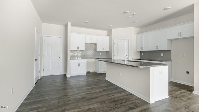 kitchen featuring dark wood-type flooring, backsplash, a kitchen island with sink, and white cabinets