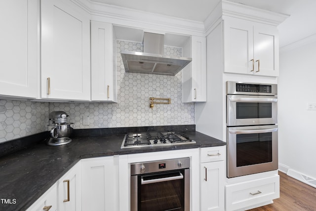 kitchen featuring decorative backsplash, wall chimney exhaust hood, stainless steel appliances, and white cabinetry