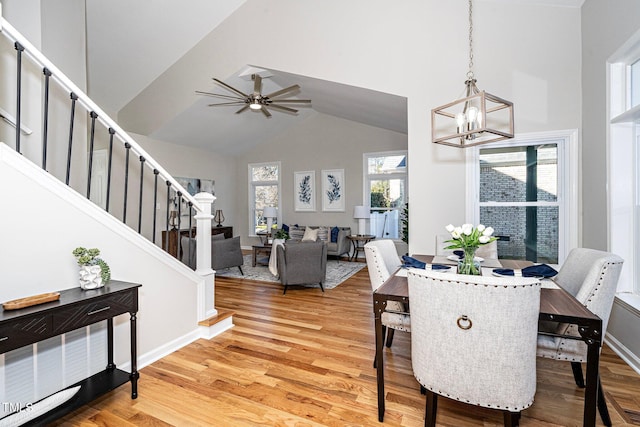 dining area with ceiling fan with notable chandelier, hardwood / wood-style flooring, and high vaulted ceiling