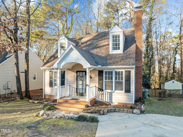 new england style home featuring a front yard and a shed