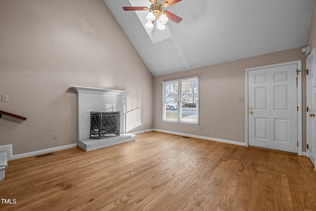 unfurnished living room with a skylight, ceiling fan, a fireplace, high vaulted ceiling, and light hardwood / wood-style flooring