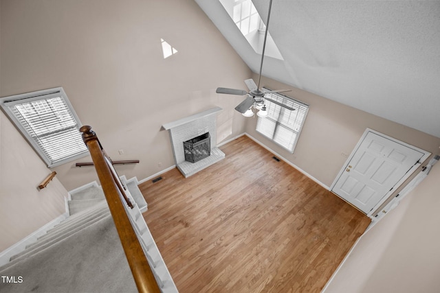 living room featuring high vaulted ceiling, ceiling fan, a brick fireplace, and light wood-type flooring