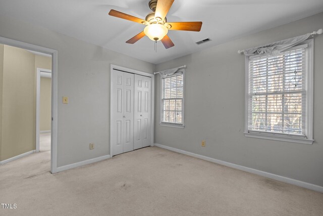 unfurnished bedroom featuring ceiling fan, light colored carpet, and a closet