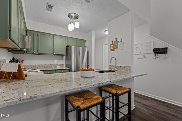 kitchen with green cabinets, sink, stainless steel fridge, light stone counters, and kitchen peninsula