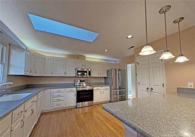 kitchen with a skylight, sink, hanging light fixtures, stainless steel appliances, and white cabinets