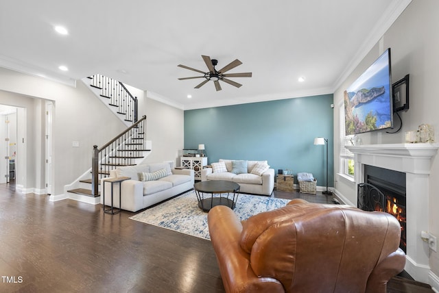 living room with a ceiling fan, wood finished floors, baseboards, a warm lit fireplace, and stairs