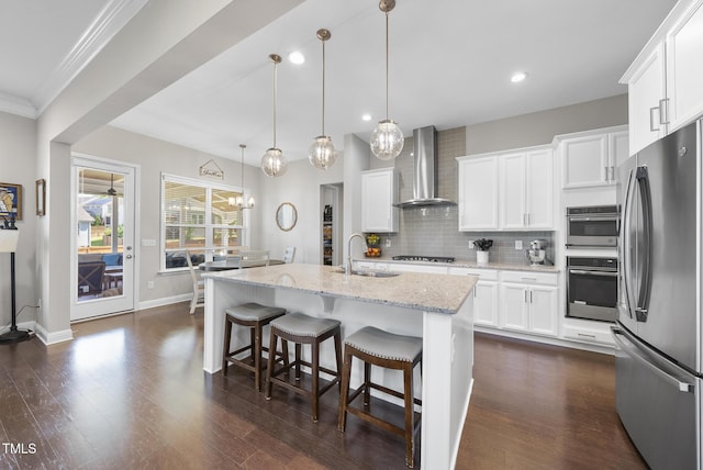kitchen featuring backsplash, a sink, light stone counters, stainless steel appliances, and wall chimney exhaust hood