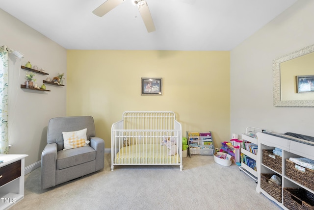 carpeted bedroom with a crib and ceiling fan
