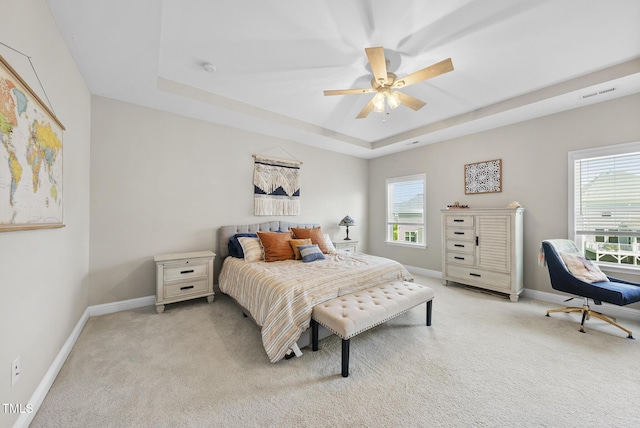 bedroom with ceiling fan, visible vents, baseboards, light carpet, and a tray ceiling