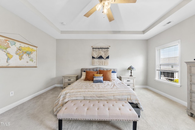 bedroom with a tray ceiling, light carpet, and baseboards