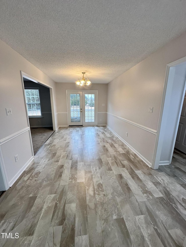 empty room featuring a notable chandelier, wood-type flooring, and a textured ceiling