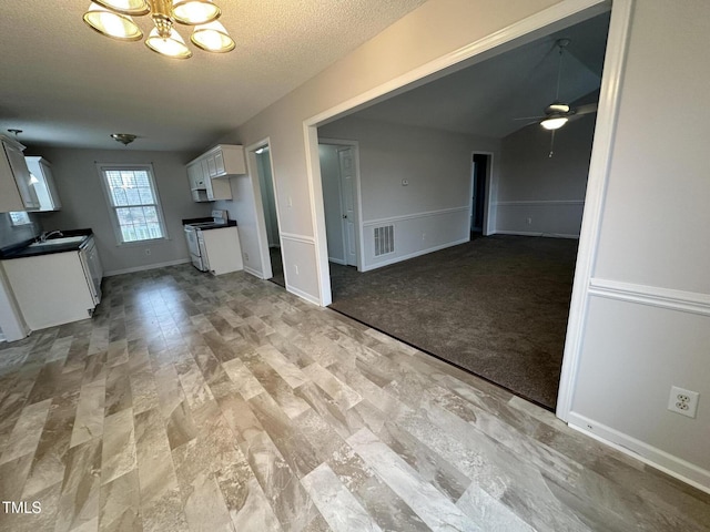 unfurnished living room featuring ceiling fan with notable chandelier, light carpet, and a textured ceiling